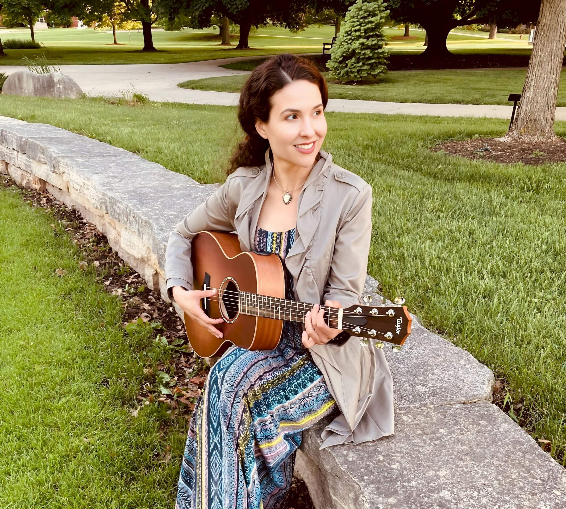 Michelle Ptacek holding a guitar sitting on rock wall.